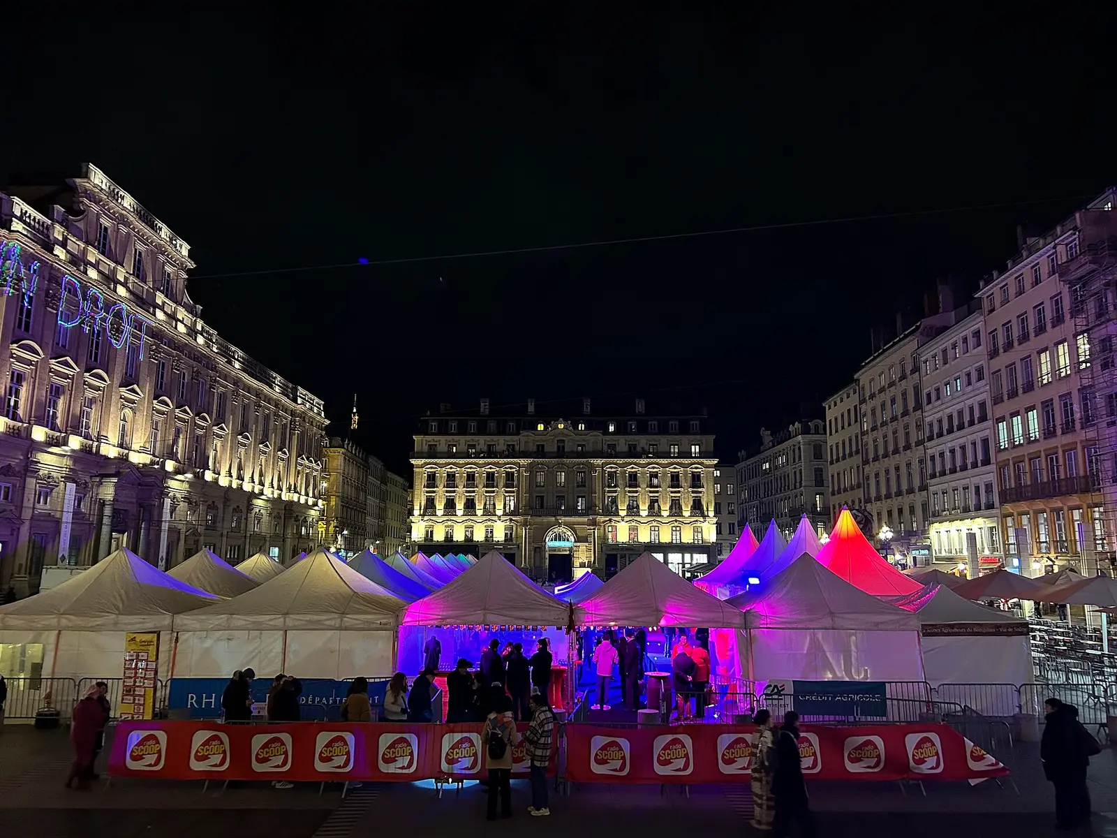 Lit marquees on a city square at night during a Beaujolais Nouveau celebration in Lyon