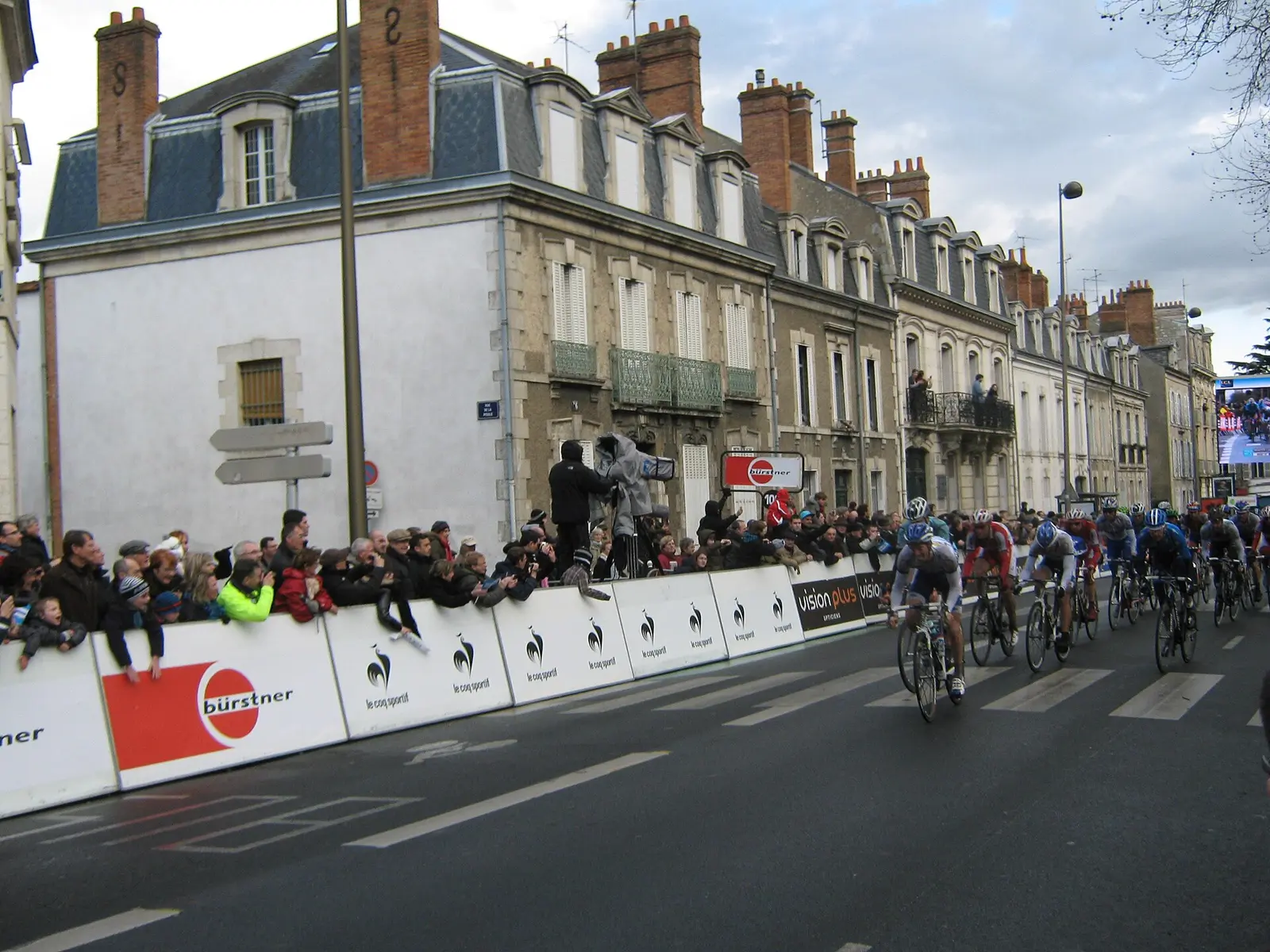 Paris-Nice peloton racing along a town street lined with spectators